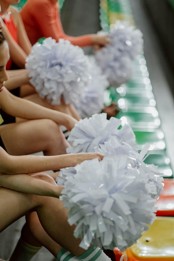 Be Your Cheerleader 1 A group of cheerleaders holding pom poms while sitting on colorful stadium bleachers. be your cheerleader