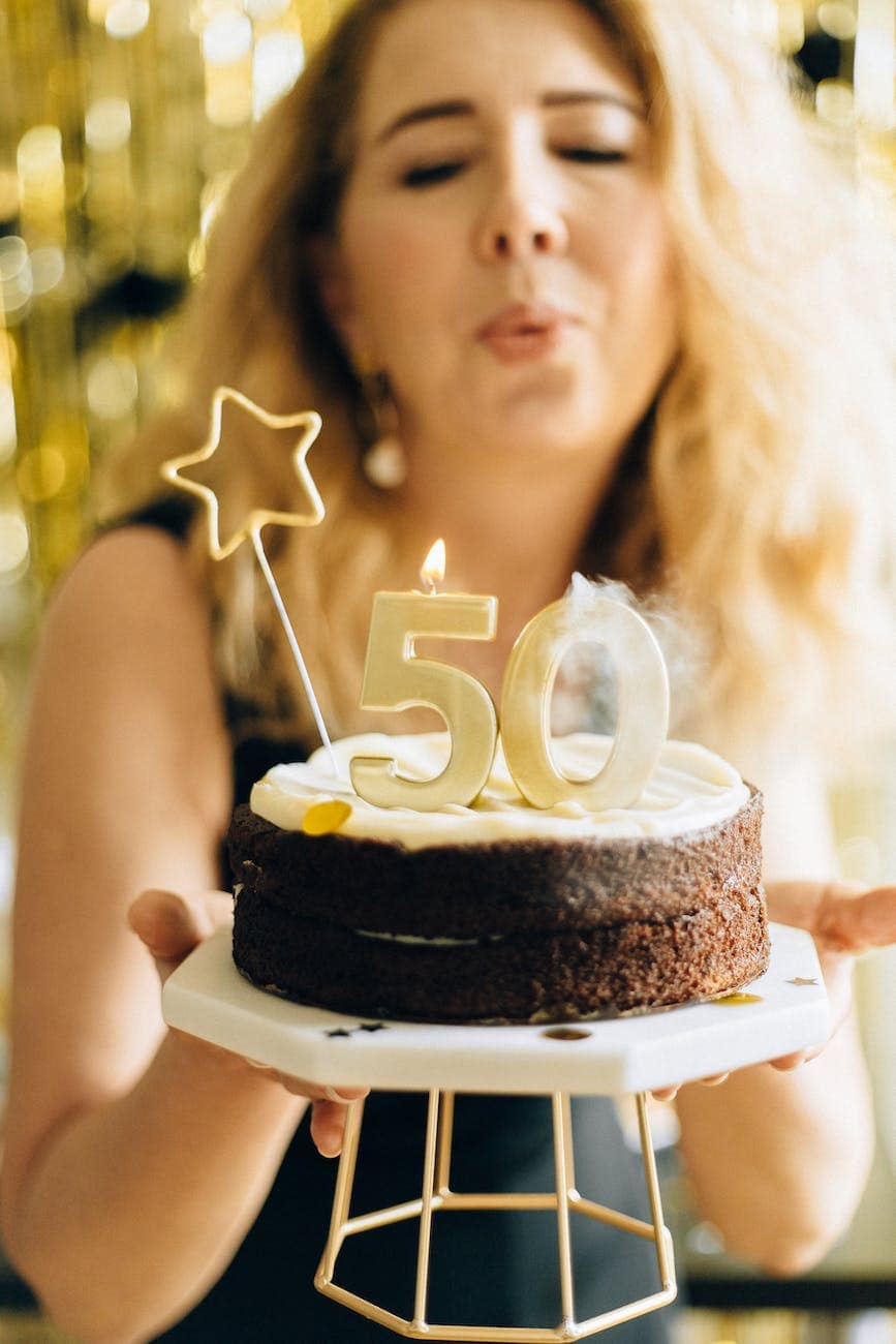 Sad About Turning 50 this Year? Read this. 1 woman in black top holding white and black cake